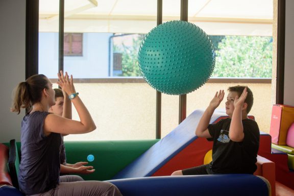 Une éducatrice lance un énorme ballon à un enfant en salle de motricité